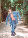 A girl with two braids in a plaid shirt with oversleeves and oversized jeans stands in a pose in a park on a green alley Royalty Free Stock Photo