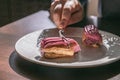 Girl breaks off a juicy delicious berry eclair with a fork. Appetizing desserts, sunny morning in a coffee shop