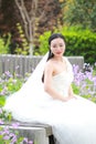 Girl bride in wedding dress with elegant hairstyle, with white wedding dress Sitting on the bench next to the fence Royalty Free Stock Photo