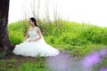 Girl bride in wedding dress with elegant hairstyle, with white wedding dress Sitting in the grass by the river Royalty Free Stock Photo