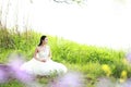 Girl bride in wedding dress with elegant hairstyle, with white wedding dress Sitting in the grass by the river Royalty Free Stock Photo