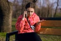 A girl in a bright jacket sits on a park bench and talks on the phone Royalty Free Stock Photo