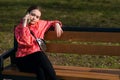 A girl in a bright jacket sits on a park bench and talks on the phone Royalty Free Stock Photo