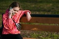 A girl in a bright jacket sits on a park bench and talks on the phone Royalty Free Stock Photo