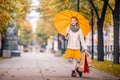 Girl with a bright jelly umbrella and with shopping guide walks along the autumn city boulevard smiling happily Royalty Free Stock Photo