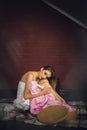 Girl with bright makeup, in a white dress, sits on the floor in a dark room against a brick wall Royalty Free Stock Photo