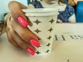 A girl with a bright, pink manicure holds a cup of coffee in her hands. long pink nails. sunburnt hand. girl drinking from a paper Royalty Free Stock Photo