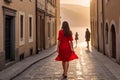 A girl in a bright red dress walks along the ancient streets with a paved road. Generative AI