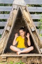 A girl in a bright yellow t-shirt sits in a small hut