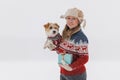 girl in a brown coat gives a Jack Russell Terrier a gift on a white background during a blizzard. The dog sits on the hands of a