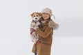 A girl in a brown coat and a jack russell terrier stand on a white background during a blizzard. The dog sits on the hands of a