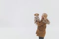 A girl in a brown coat and a jack russell terrier stand on a white background during a blizzard. The dog sits on the hands of a