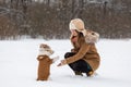 A girl in a brown hat with earflaps and a dog on the background of trees in the park. Portrait of a Jack Russell Terrier dressed