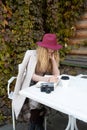A girl in a burgundy hat sits at a table in a street cafe, drinks coffee and writes in a notebook Royalty Free Stock Photo