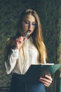 A girl in business clothes and glasses holds a black folder in her hands.