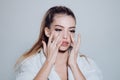 Girl on busy face in bathrobe covering face with cream, grey background. Woman with healthy skin. Lady cares about