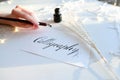 Female master of lettering of ink writes word on paper, sitting Royalty Free Stock Photo