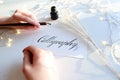 Female master of lettering of ink writes word on paper, sitting Royalty Free Stock Photo