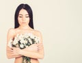 Girl on calm face stands naked and holds chamomile flowers in front of chest. Lady covers breasts with flowers, isolated