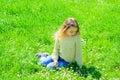 Girl on calm or sad face spend leisure outdoors. Girl sits on grass at grassplot, green background. Child enjoy spring