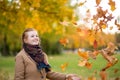 Girl in a camel coat in autumn park smiles and catches falling leaves Royalty Free Stock Photo