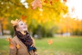 Girl in a camel coat in autumn park smiles and catches falling leaves Royalty Free Stock Photo