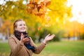 Girl in a camel coat in autumn park smiles and catches falling leaves Royalty Free Stock Photo