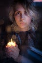 Girl with a candle. Portrait through the glass. Biliki, reflection, bokeh. Prayer for relatives. Conceptual photography: the theme