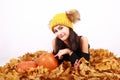 Girl in cap with bobbles lying on autumn leaves by pumpkins Royalty Free Stock Photo