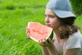 Girl in a cap, lies on green grass and holds a piece of watermelon, there is a place for inscription, close-up