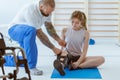 Girl after car accident with orthosis on the leg exercises on blue mat in the company of physiotherapist