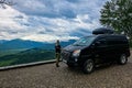 A girl at a car on the background of a view of the Lago-Naki plateau in Adygea. The Caucasus Mountains. Russia 2021