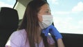 A girl in a car wearing a medical mask and blue gloves to prevent the spread of COVID-19. Riding a woman wearing a