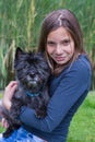 Girl carrying black dog on arm in nature