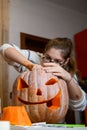 A girl carving big orange pumpkin into jack-o-lantern for Halloween holiday decoration at kitchen. Decoration for party Royalty Free Stock Photo