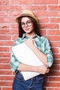 Girl in casual clothes, hat and eyeglasses posing, smiling and with close laptop in hands,