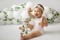 A girl celebrates her first birthday and eats a birthday cake. Decorations for a child`s birthday made of balloons and ivy Royalty Free Stock Photo
