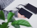 A girl charges her phone at a Desk in the office or at home. Power bank and smartphone. Black powerbank, cable and cell phone