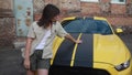 Girl Charlie Watson stands near yellow car with the autobot logo or robot transformer Bumblebee