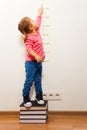 Girl checking height on growth chart at four books