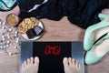 Girl checks her weight on digital scales. Sign omg! on balance surrounded by cup of coffee, sweets and female clothes and shoes