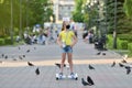 Girl child in a black protective mask rides on a hoverboard past pigeons in a park during the COVID-19 pandemic