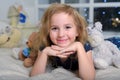 Child blonde in a blue dress lies on the bed with many toy bears Royalty Free Stock Photo