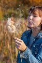 Girl child blows on a cattail in hand and fluff flies in her face