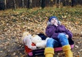 A girl child in a blue hat and yellow boots sits in a pink suitcase with soft toys and looks wistfully to the side. Autumn, dry Royalty Free Stock Photo