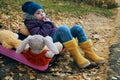 A girl child in a blue hat and yellow boots sits in a pink suitcase with soft toys and looks wistfully to the side. Autumn, dry Royalty Free Stock Photo