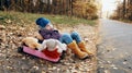 A girl child in a blue hat and yellow boots sits in a pink suitcase with soft toys and looks wistfully to the side. Autumn, dry Royalty Free Stock Photo