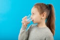 Girl child drinks pure mineral water from glass, portrait on blue background