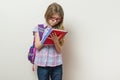 Girl child elementary school student wearing glasses with a backpack writing in her notebook. Bright school wall background