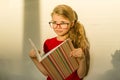 Girl child elementary school student wearing glasses is holding a textbook and dreamily smiling looking forward Royalty Free Stock Photo